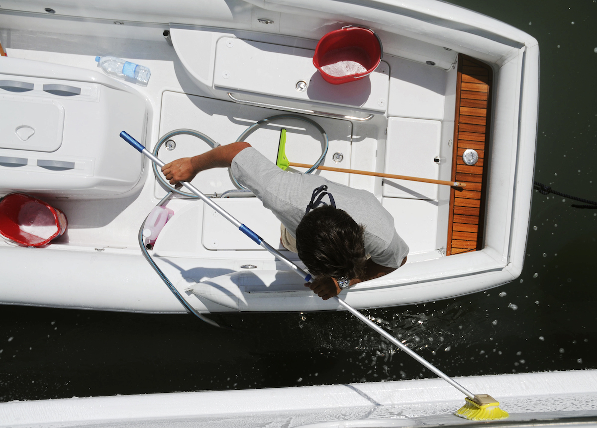 Overhead view of a professional detailer cleaning a white boat deck with a long-handled brush, demonstrating expert boat detailing.