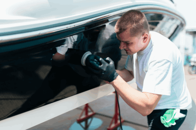 Expert detailer wearing black gloves polishing the black hull of a boat, creating a mirror-like reflection.