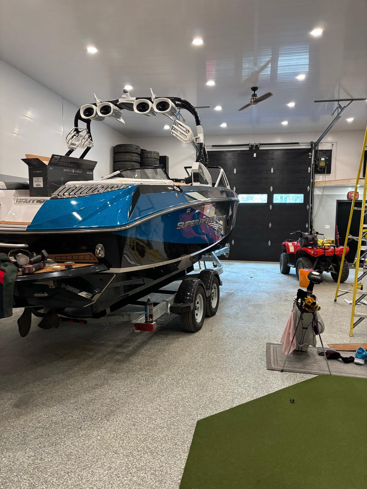 Sleek blue and black wake boat on trailer inside a garage, gleaming after professional detailing by True North Detailing Muskoka.