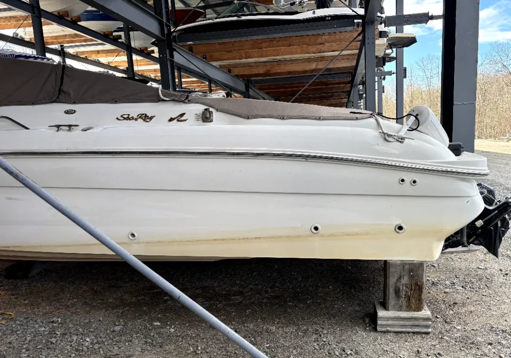 Dirty white Sea Ray boat hull with a brown waterline stain, out of water on stands, at a Muskoka marine storage facility.