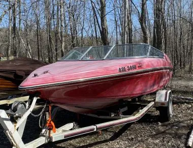 Heavily faded and oxidized red boat on a trailer, showing chalky gel coat before professional restoration.