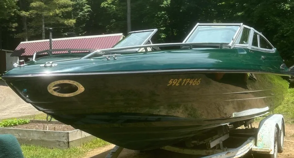Sleek green boat with high-gloss hull on a trailer outdoors, reflecting trees after professional detailing by True North Detailing Muskoka.